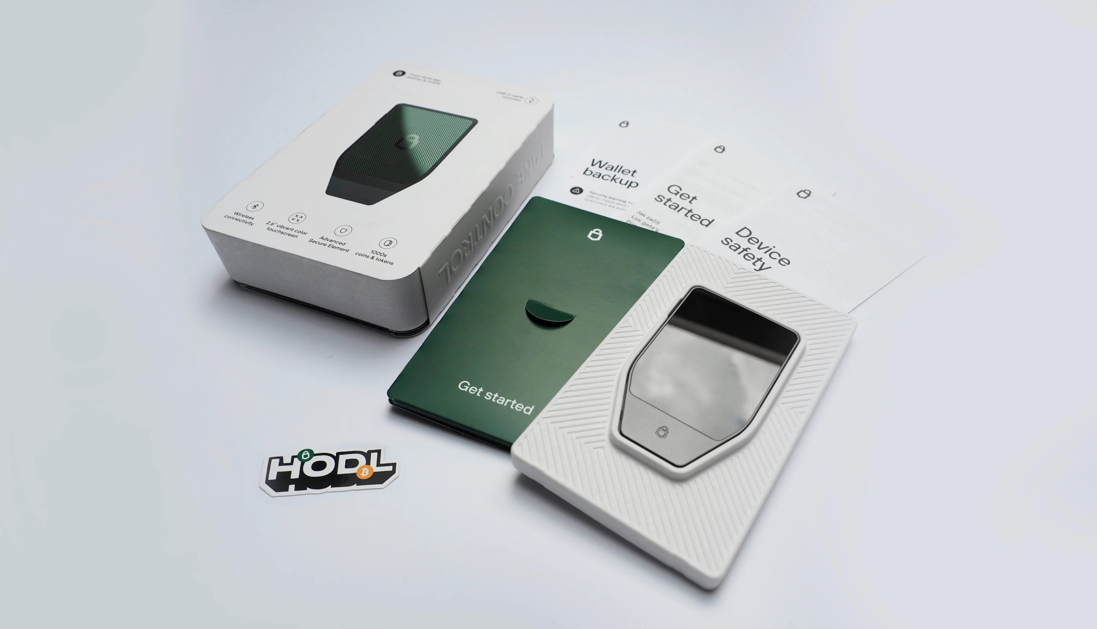 The full unboxing laid out — box, get-started card, the device in its tray, the fold-out manual and a “Hodl” sticker.
